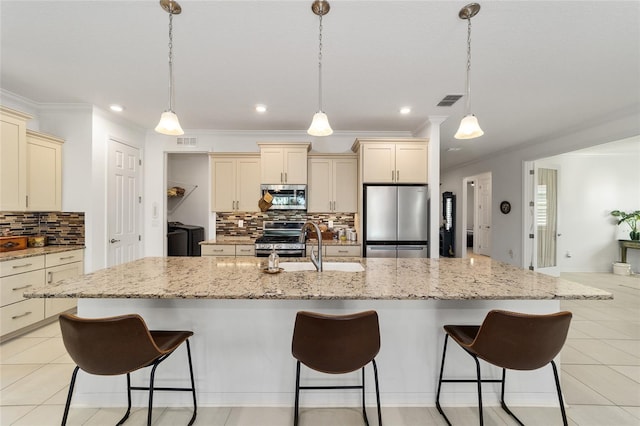 kitchen featuring a large island with sink, cream cabinets, pendant lighting, appliances with stainless steel finishes, and washing machine and clothes dryer