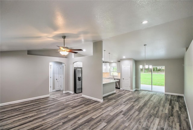 unfurnished living room featuring dark wood-type flooring, a textured ceiling, vaulted ceiling, and ceiling fan with notable chandelier