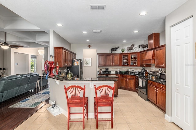 kitchen featuring appliances with stainless steel finishes, a kitchen bar, ceiling fan, dark stone countertops, and light tile patterned floors