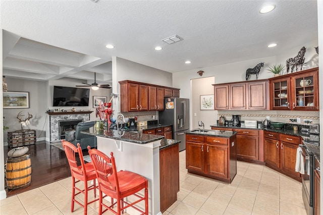 kitchen with a kitchen breakfast bar, dark stone countertops, a high end fireplace, a center island, and appliances with stainless steel finishes