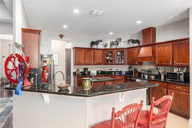 kitchen featuring decorative backsplash, stainless steel appliances, dark stone countertops, a kitchen bar, and a textured ceiling