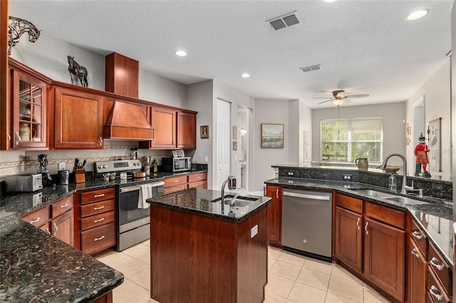 kitchen featuring custom range hood, a center island with sink, sink, appliances with stainless steel finishes, and a textured ceiling