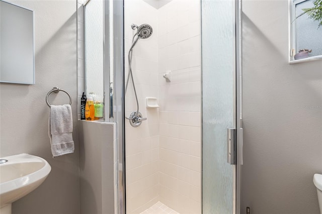 bathroom featuring a shower with door, toilet, and sink