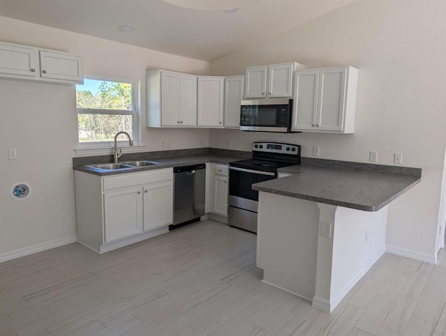 kitchen with kitchen peninsula, stainless steel appliances, sink, vaulted ceiling, and white cabinetry