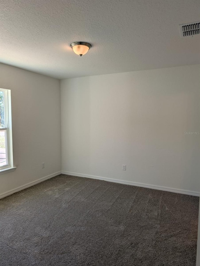 empty room with a textured ceiling and dark carpet