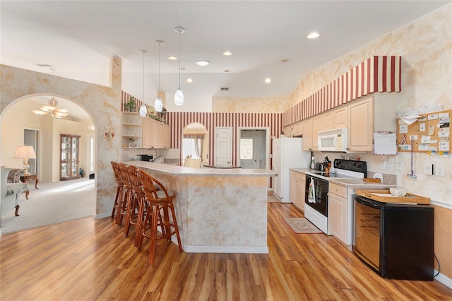 kitchen featuring a breakfast bar area, light hardwood / wood-style flooring, decorative light fixtures, and white appliances