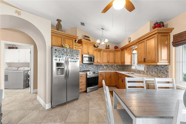 kitchen featuring lofted ceiling, appliances with stainless steel finishes, washing machine and dryer, pendant lighting, and sink