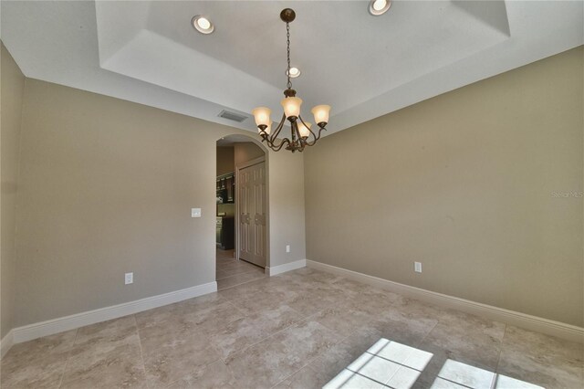 tiled empty room featuring a tray ceiling and a chandelier