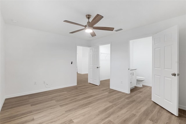 unfurnished bedroom featuring ceiling fan, light wood-type flooring, a spacious closet, connected bathroom, and a closet