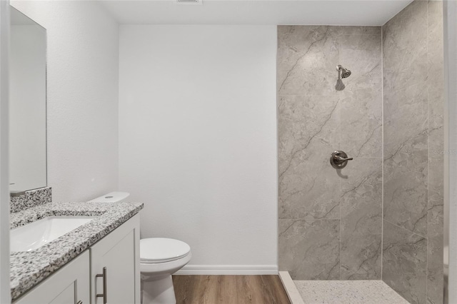 bathroom featuring toilet, tiled shower, hardwood / wood-style flooring, and vanity