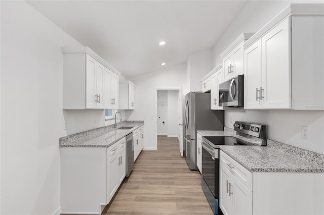 kitchen with white cabinetry, stainless steel appliances, vaulted ceiling, light stone counters, and sink