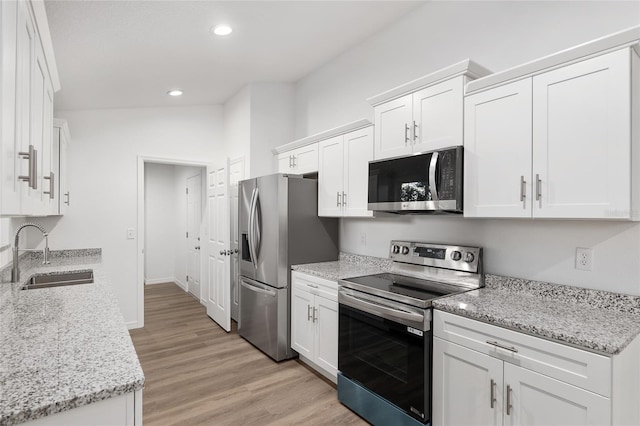 kitchen with sink, light wood-type flooring, light stone countertops, stainless steel appliances, and white cabinets