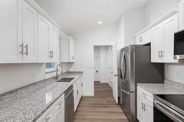 kitchen with light stone countertops, white cabinets, appliances with stainless steel finishes, lofted ceiling, and sink