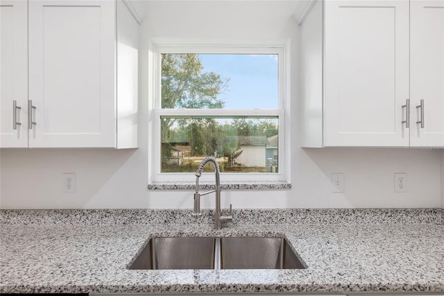 kitchen with light stone countertops, white cabinets, and sink