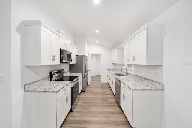 kitchen featuring lofted ceiling, light hardwood / wood-style flooring, light stone countertops, stainless steel appliances, and white cabinets