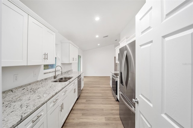 kitchen featuring white cabinets, appliances with stainless steel finishes, sink, light stone counters, and light hardwood / wood-style flooring