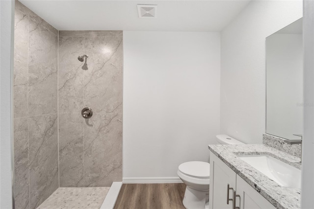 bathroom with wood-type flooring, toilet, vanity, and tiled shower