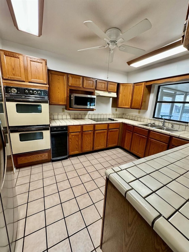 kitchen featuring tile countertops, sink, ceiling fan, light tile patterned flooring, and double oven