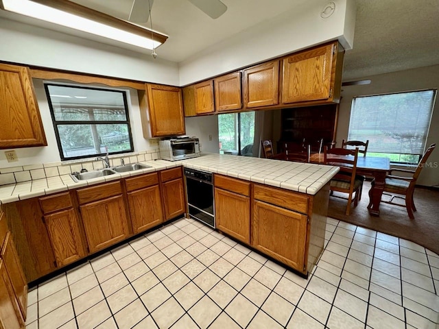 kitchen featuring dishwasher, tile countertops, kitchen peninsula, and sink