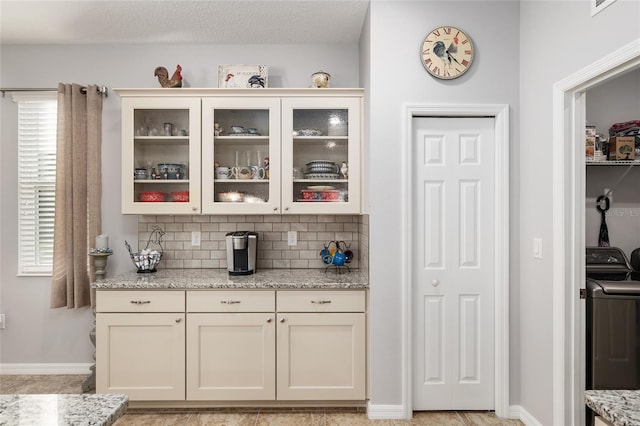 bar with tasteful backsplash, washer / clothes dryer, light stone counters, and a textured ceiling