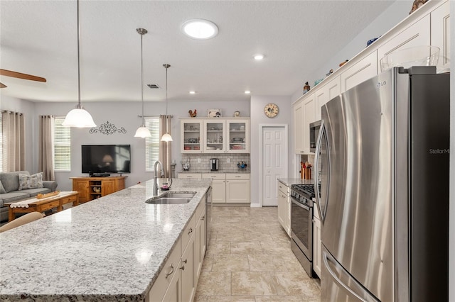 kitchen with sink, decorative light fixtures, decorative backsplash, a center island with sink, and appliances with stainless steel finishes