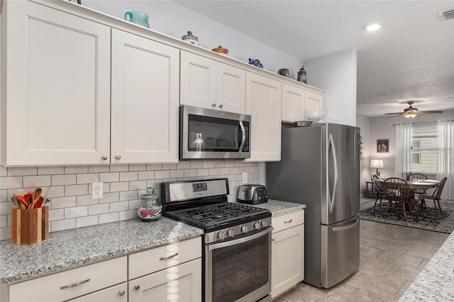 kitchen featuring ceiling fan, light stone countertops, tasteful backsplash, white cabinets, and appliances with stainless steel finishes