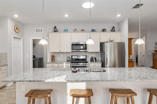 kitchen with tasteful backsplash, separate washer and dryer, pendant lighting, a kitchen bar, and appliances with stainless steel finishes