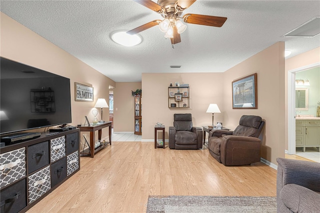 living room with light hardwood / wood-style floors, a textured ceiling, and ceiling fan