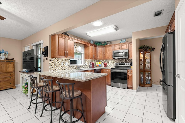 kitchen featuring appliances with stainless steel finishes, a textured ceiling, kitchen peninsula, and a kitchen breakfast bar