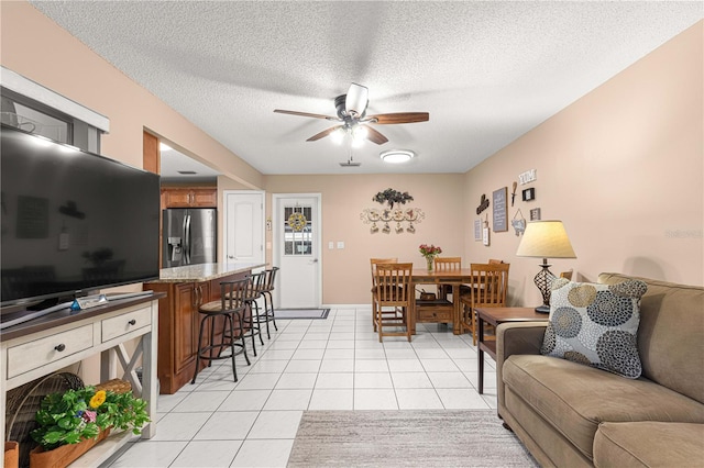 living room featuring ceiling fan, a textured ceiling, and light tile patterned flooring