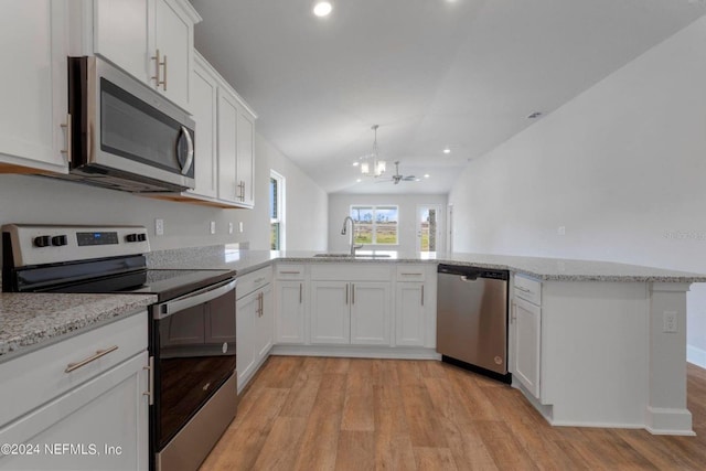 kitchen with kitchen peninsula, appliances with stainless steel finishes, sink, white cabinetry, and lofted ceiling