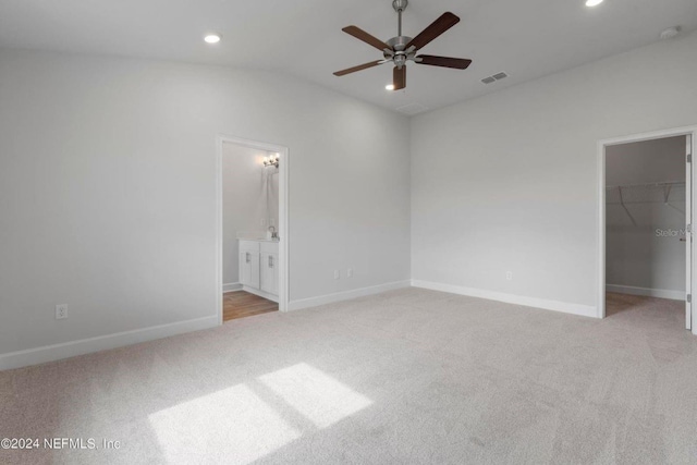 unfurnished bedroom featuring ensuite bath, ceiling fan, a spacious closet, vaulted ceiling, and light carpet