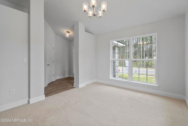 carpeted spare room featuring an inviting chandelier