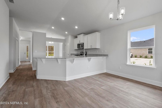 kitchen with stainless steel microwave, hanging light fixtures, white cabinetry, a peninsula, and a kitchen breakfast bar