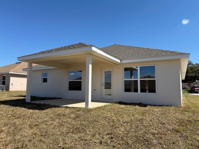 back of property with roof with shingles, a patio, a lawn, and stucco siding