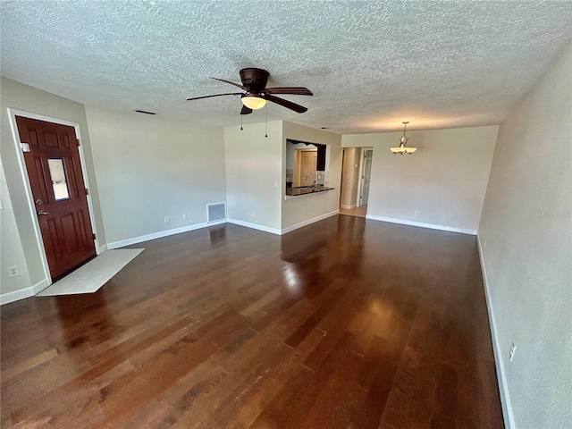 unfurnished living room with ceiling fan with notable chandelier, dark hardwood / wood-style flooring, and a textured ceiling