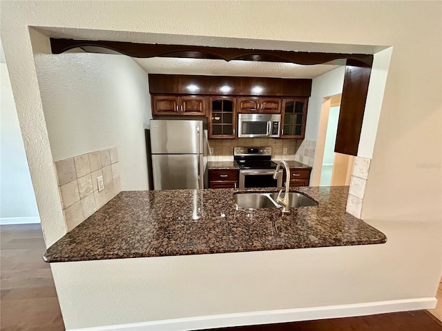 kitchen featuring stainless steel appliances, dark stone counters, dark brown cabinets, sink, and decorative backsplash