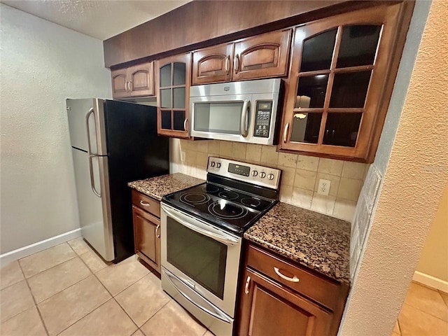 kitchen with appliances with stainless steel finishes, dark stone counters, tasteful backsplash, and light tile patterned floors