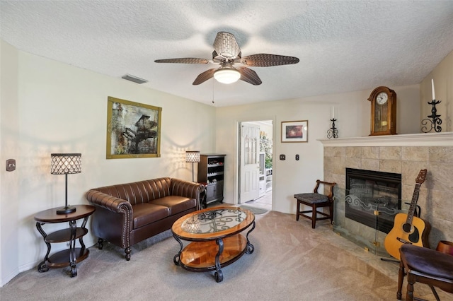 carpeted living room with ceiling fan, a textured ceiling, and a tiled fireplace