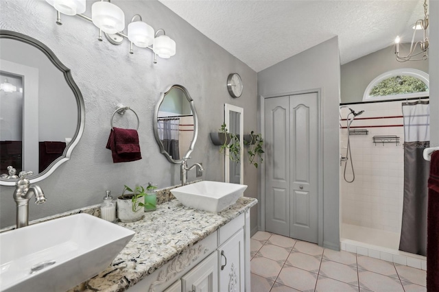 bathroom with vanity, vaulted ceiling, tile patterned flooring, a textured ceiling, and tiled shower