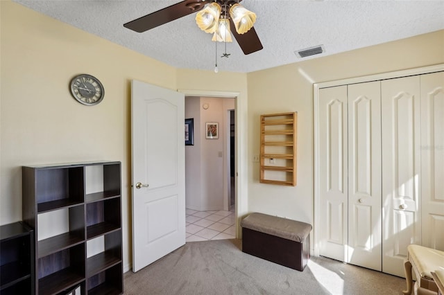 bedroom with ceiling fan, a closet, light colored carpet, and a textured ceiling