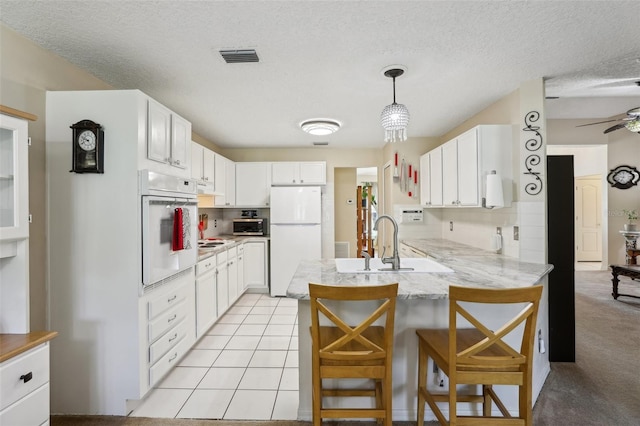 kitchen featuring white cabinetry, hanging light fixtures, kitchen peninsula, white appliances, and a breakfast bar area