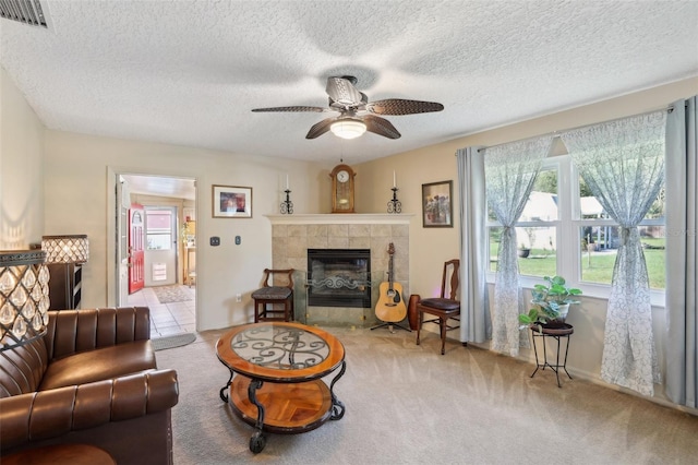 carpeted living room featuring a tiled fireplace, ceiling fan, and a textured ceiling