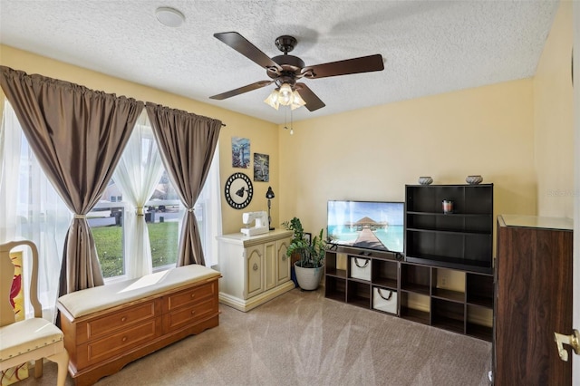 living area with a textured ceiling, light colored carpet, and ceiling fan