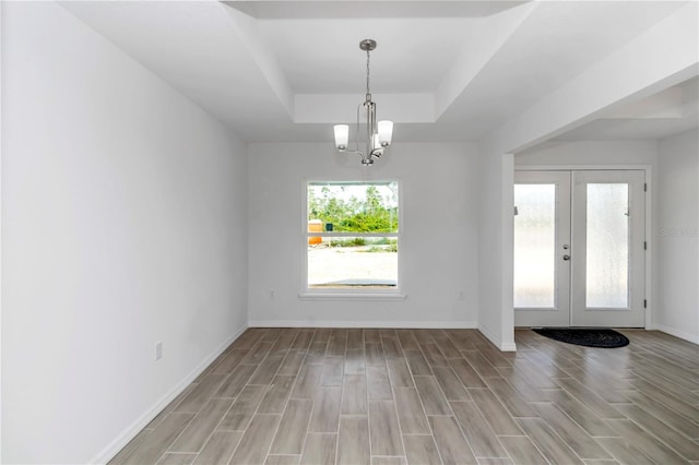 interior space with an inviting chandelier, french doors, a raised ceiling, and light hardwood / wood-style flooring