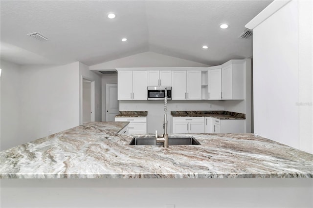 kitchen with sink, kitchen peninsula, light stone counters, lofted ceiling, and white cabinets