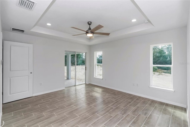 spare room with ceiling fan, plenty of natural light, light hardwood / wood-style flooring, and a tray ceiling