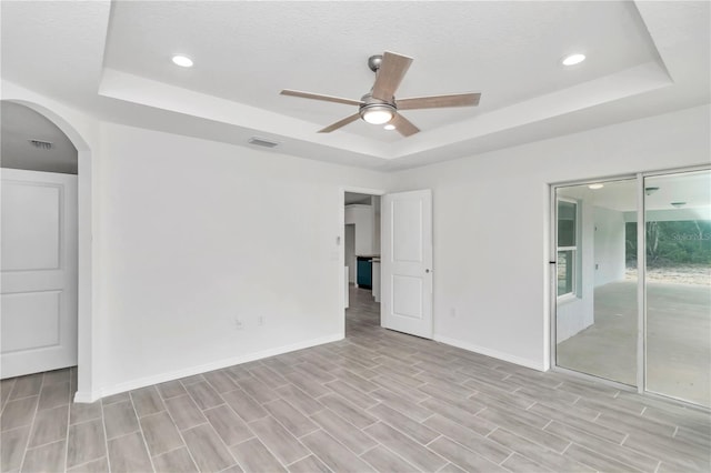 unfurnished room with light wood-type flooring, ceiling fan, and a raised ceiling