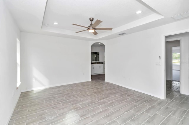 spare room featuring light hardwood / wood-style flooring, ceiling fan, and a tray ceiling