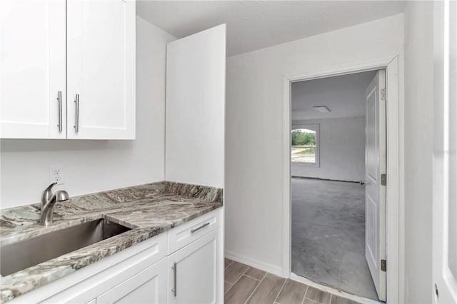 kitchen featuring light wood-type flooring, light stone countertops, sink, and white cabinets